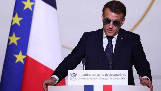 French President Emmanuel Macron, wearing sunglasses, delivers a speech during a ceremony to award the Chevalier of the French Order of Merit to Ali Akbar, who hawks newspapers around the streets of Saint-Germain-des-Pres in the French capital for 50