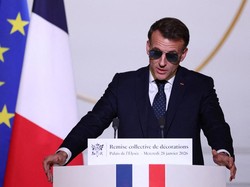 French President Emmanuel Macron, wearing sunglasses, delivers a speech during a ceremony to award the Chevalier of the French Order of Merit to Ali Akbar, who hawks newspapers around the streets of Saint-Germain-des-Pres in the French capital for 50