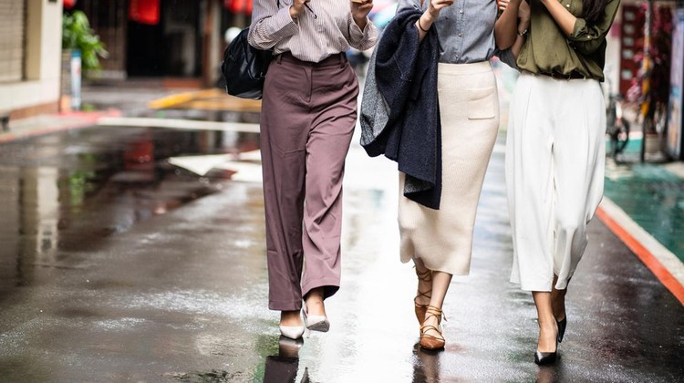 Three female friends walking on the street&comma; drinking coffee on the move&comma; talking and smiling lively on rainy day