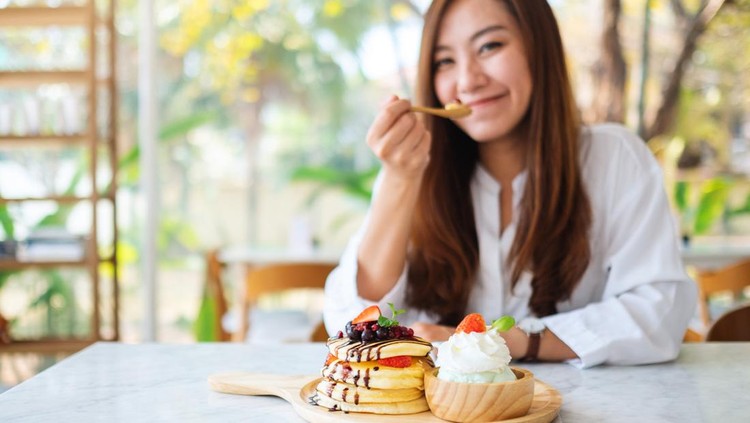 A beautiful asian woman eating ice cream and a mixed berries pancakes with whipped cream by wooden spoon