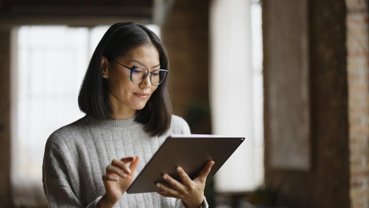 Smiling Chinese businesswoman reading her plans on digital tablet in the office&period;