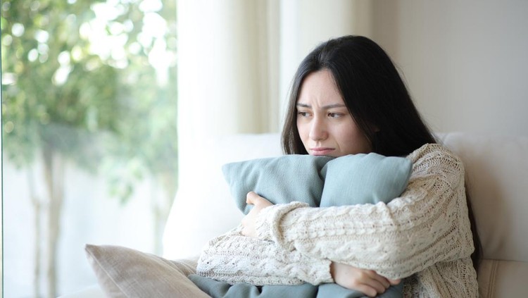 Sad asian woman complaining hugging pillow at home