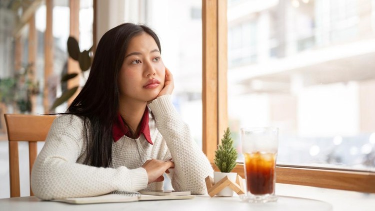 An asian woman is putting her hand under the chin&comma; looking bored or unhappy while waiting for someone at the round marble table&period; Study or Working in the cafe&period;