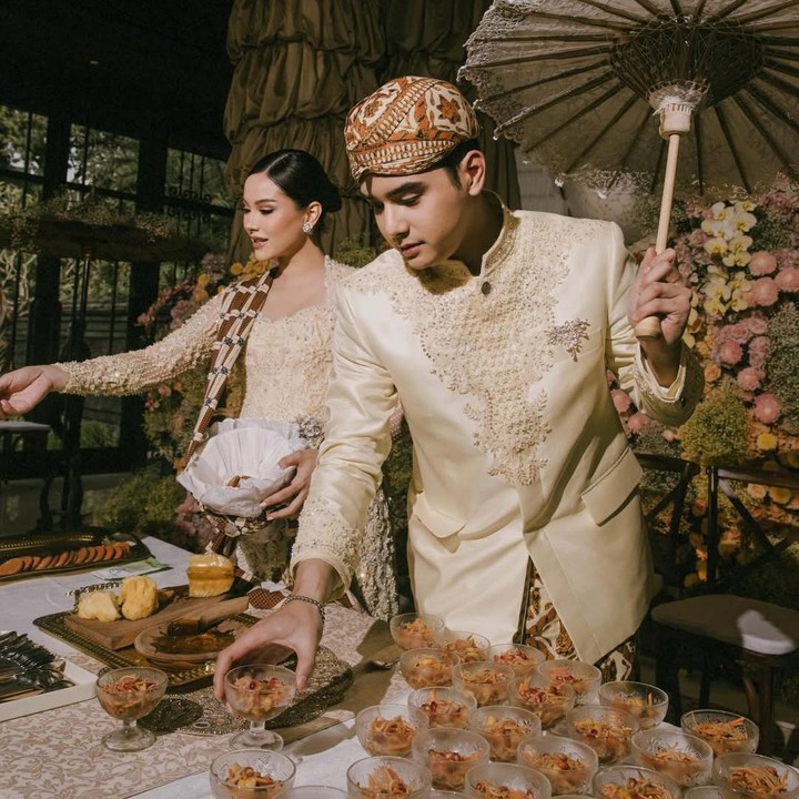 <p>Di acara ini, Alyssa dan Al Ghazali juga menjalani tradisi 'menjual' asinan buah untuk semua tamu yang hadir. Dalam momen yang dibagikan di Instagram, tampak Alyssa sibuk menjajakan asinan, sementara suaminya memayungi sambil menata gelas di meja. (Foto: Instagram @alyssadaguise)</p>