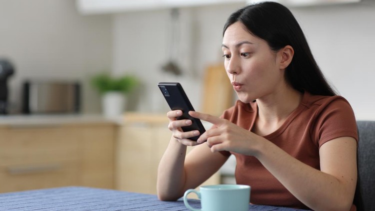 Surprised asian woman using smart phone in a kitchen at home