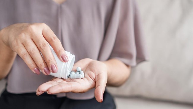 close up of woman's hand holding a bottle of medicine while taking vitamin pills or supplements such as probiotics, zinc, or magnesium to support her health and well being