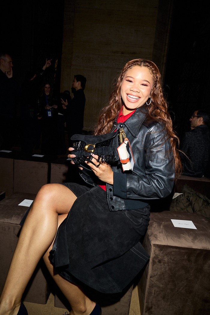 Storm Reid mengangkat pesona permainan tekstur dalam satu look. Namun tak semata dari kombinasi material sarat tekstur saja, dari segi warna, sang aktris membiarkan warna merah kemeja jadi daya tarik utama penampilan yang didominasi gelap itu/ Foto: Dok. Coach