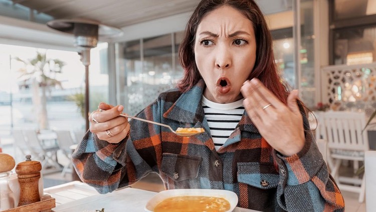 Young woman sitting at an outdoor cafe&comma; surprised by the heat and piquancy of her soup&comma; showcasing a humorous dining experience