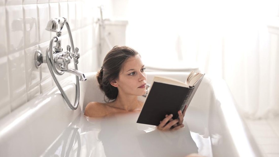young woman in bath tub reads a book