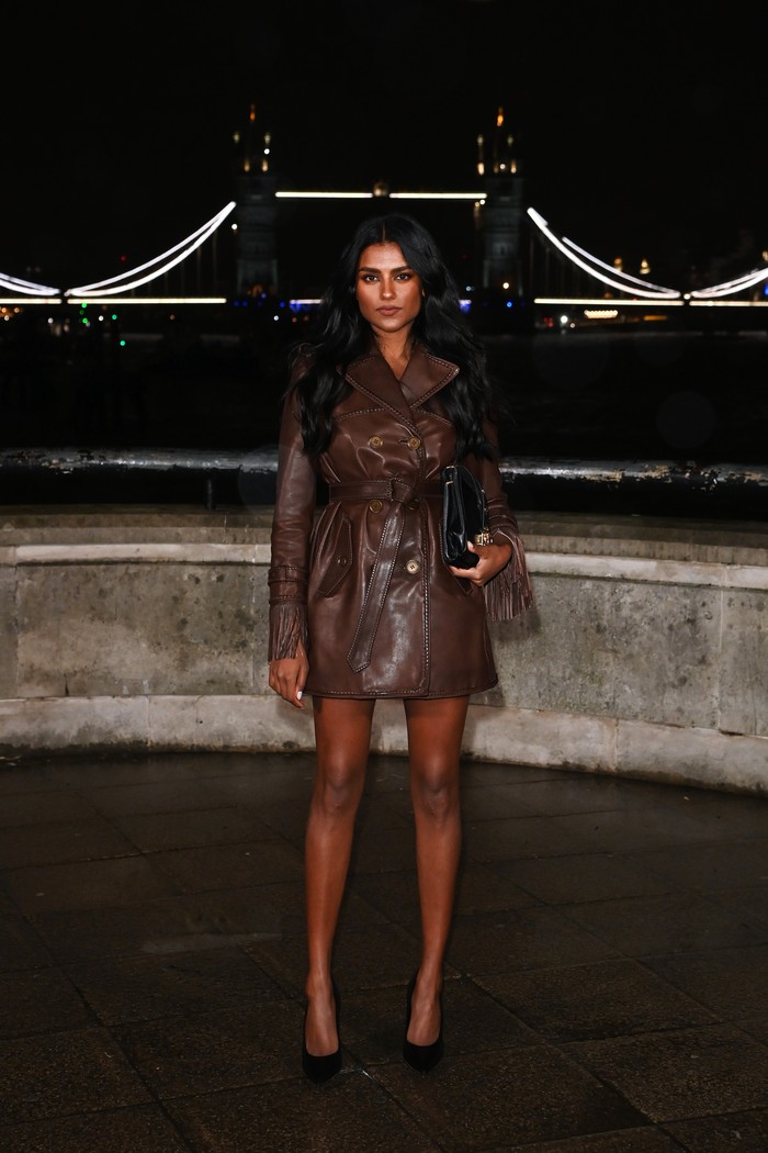 Simone Ashley menyaksikan peragaan busana Burberry Winter 2026 di London Fashion Week dalam pesona yang fierce. Jaket yang jatuh pada paha dipermanis detail kepang sepanjang pinggiran, ikat pinggang besar, dan juga aksen fringe di kedua ujung lengan. Clutch hitam dalam genggaman senada dengan pointy pumps polosnya/ Foto: Courtesy of Burberry/Dave Benett/Dave Benett