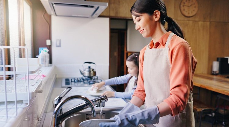 Mom&comma; girl and washing dishes in home with smile&comma; learning and helping hand for hygiene in kitchen&period; People&comma; mother and daughter with routine&comma; teaching and happy for cleaning at family house in Japan