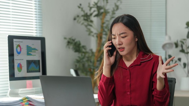 Young asian businesswoman arguing on the phone while sitting at her desk in a modern office&comma; displaying signs of frustration and stress amid her busy workday