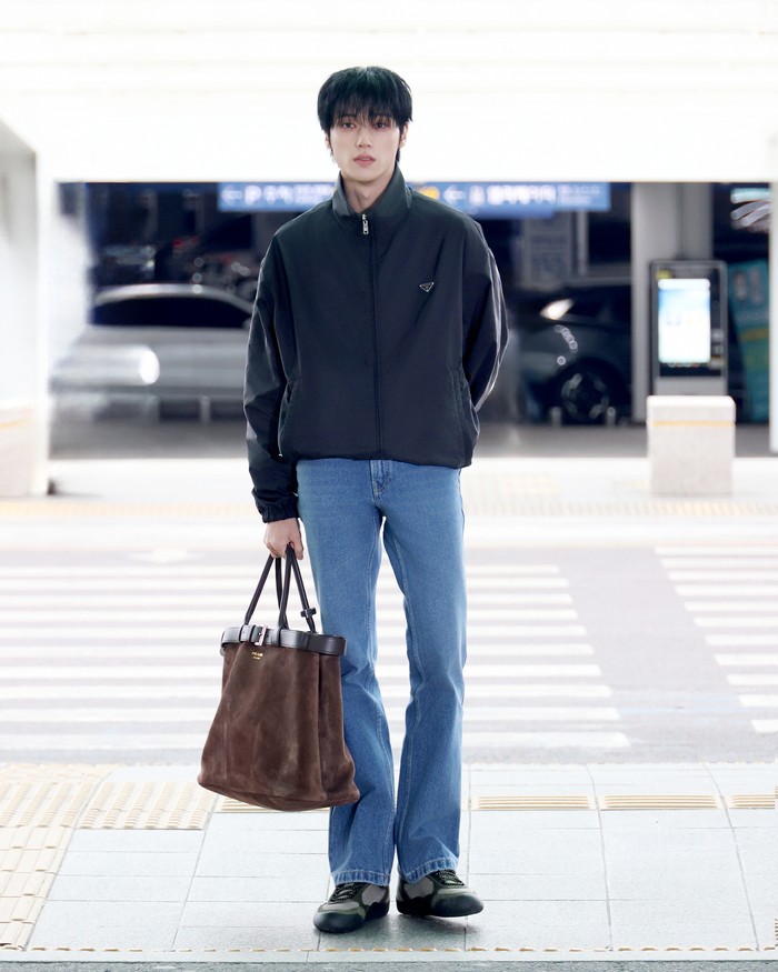 Wooyoung ATEEZ tiba di bandara dengan gaya kasual yang nyaman, Beauties. Jaket, celana jeans, dan sneakers berkesan rileks, sehingga perhatian langsung terpusat pada tas Prada Buckle dalam genggamannya/ Foto: Dok. Prada