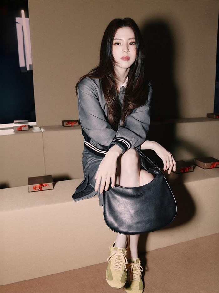 Han So Hee terlihat cantik dalam balutan rok dan jaket berwarna abu-abu, hand bag berwarna hitam, serta sepasang sepatu sneakers berwarna krem./ Foto: instagram.com/fila_korea