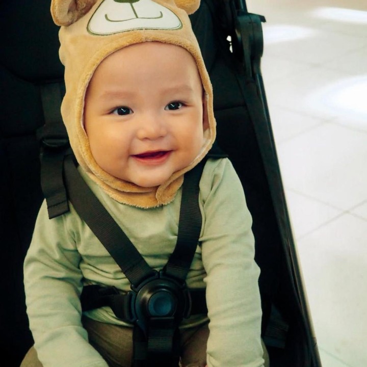 <p>Si Kecil Rayven berhasil mencuri perhatian dengan ekspresi cerianya saat duduk di <em>stroller</em>. Dalam foto tersebut, ia terlihat mengenakan baju lengan panjang dan topi beruang yang membuat penampilannya tampak semakin menggemaskan. (Foto: Instagram @ribkasugiarto)</p>