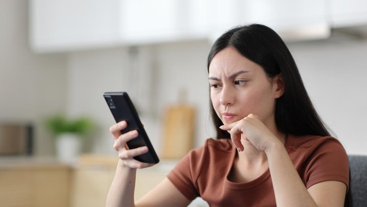 Suspicious asian woman checking phone content in the kitchen at home