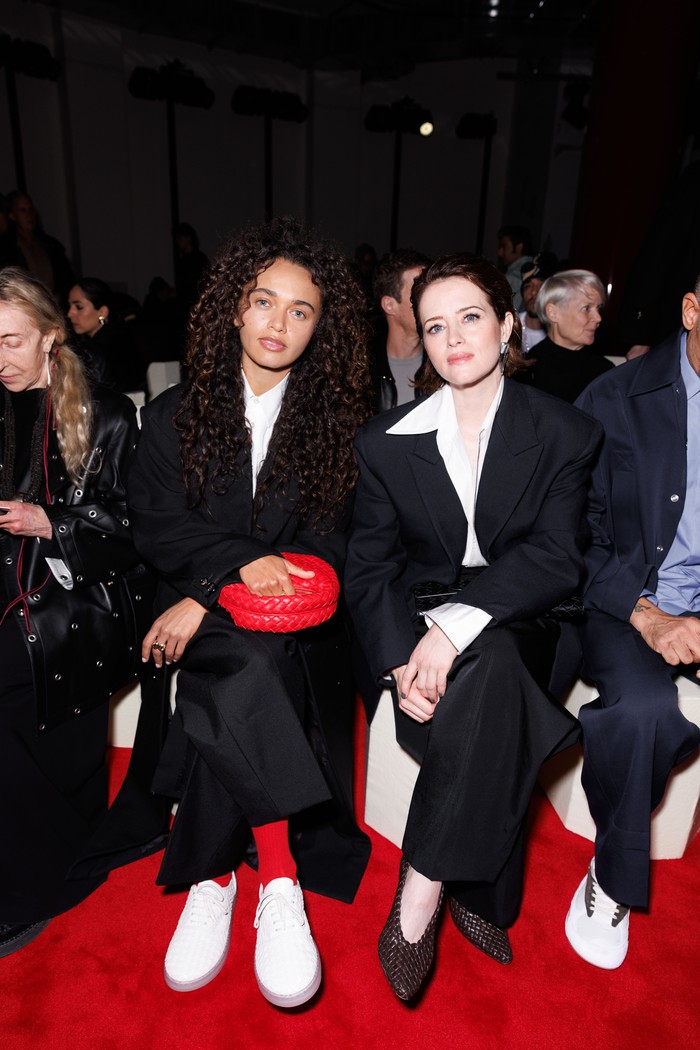 India Sleem dan Claire Foy kompak mengenakan kemeja putih dan setelan jas hitam, Beauties. Namun perbedaan paling menonjol tampak pada detail. Misalnya sneakers putih dipakai Sleem memberi sentuhan sporty, sedangkan Foy memilih nuansa chic dengan pointy heels/ Foto: Dok. Bottega Veneta