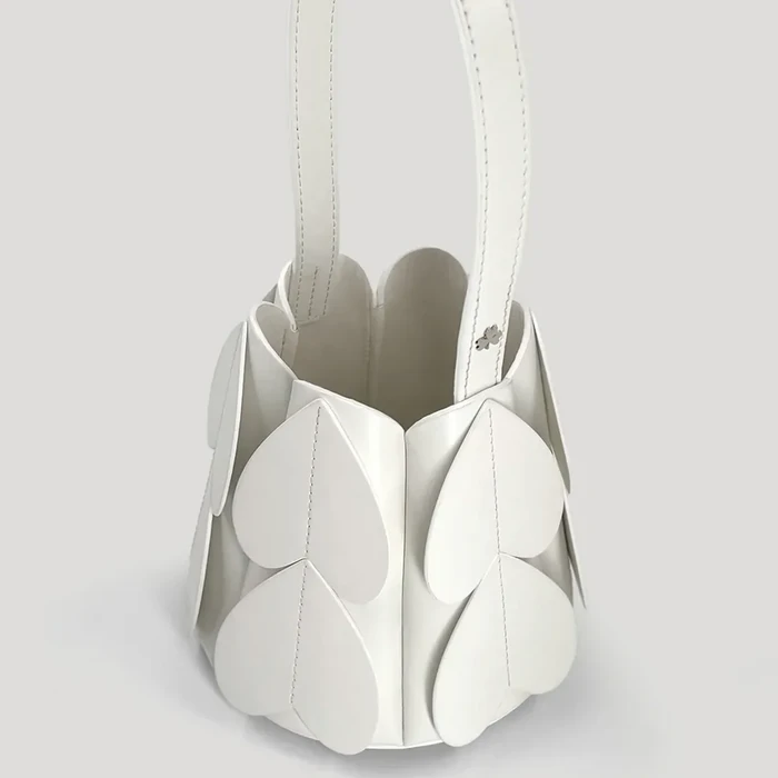 Daya tarik utama tas ini terletak pada signature leaf appliqués, yaitu aplikasi bentuk daun yang menjadi ciri khas unik dari desain Peggy Hartanto. Tas ini hadir dalam desain bucket bag dengan struktur yang kokoh.