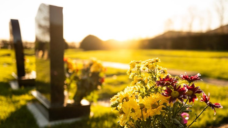 Dusk at a winter's English cemetery seen with in-focus flowers in a burial plot&period; A number of fresh marble headstones can be seen&period;