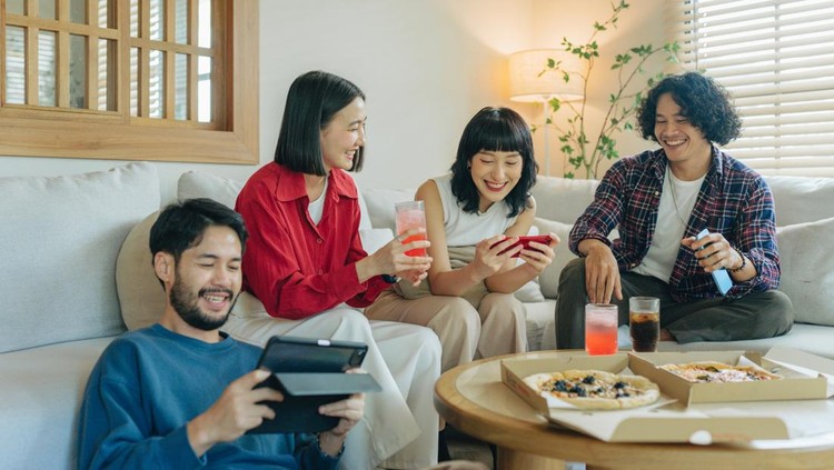 Group of friends enjoying life and having fun at home&period; Friends day in the apartment&period; Young women and young men spending time together chatting and making activities in the living room&period; Concept about lifestyle