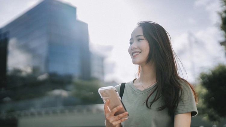 asian Chinese woman walking beside riverbank in the morning with smart phone