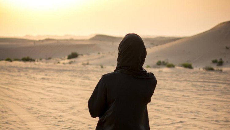 Woman in a burka Burqa walking over a middle eastern desert during sunset&period;