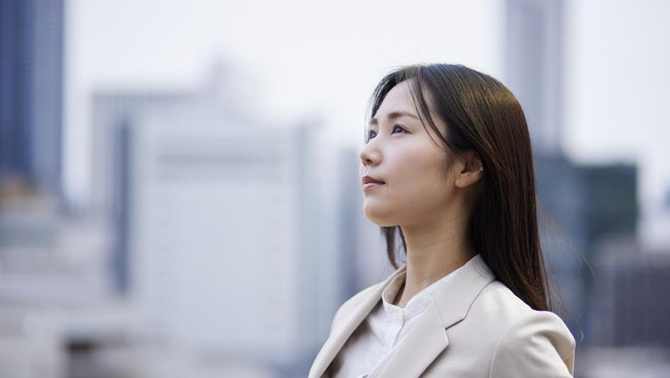 A businesswoman in a suit gazing into the distance with a group of buildings in the background