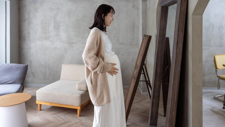 Pregnant woman standing in front of mirror in living room