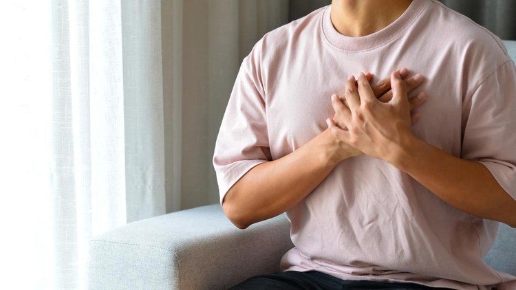 Young man sitting on sofa in the living room using both hands holding chest with symptom heart attack disease&period;He was worried because of the pain on the left side of his chest&period;