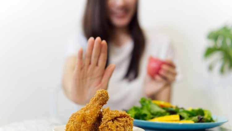 Young girl on dieting for good health concept&period; Close up female using hand reject junk food by pushing out her favorite fried chicken and choosing red apple and salad for good health&period;