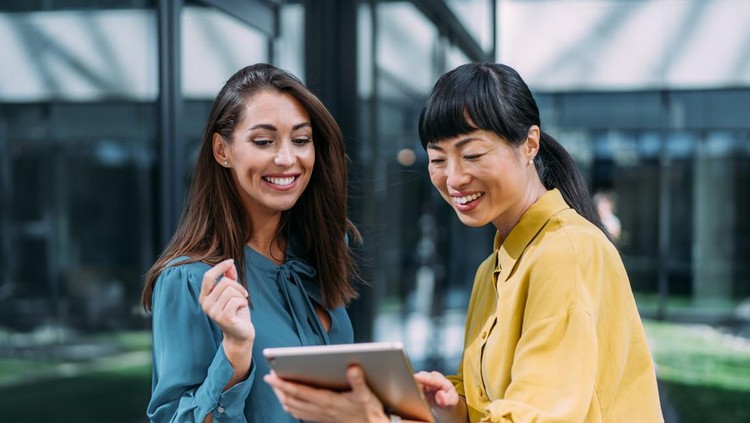 Shot of two confident female colleagues walking and talking next to an office building&period; Businesswomen in meeting using digital tablet and discussing business strategy&period; Creative business persons discussing new project and sharing ideas while walking in front of their office building&period;