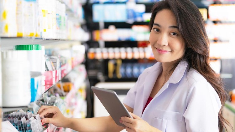 Female pharmacist taking a medicine from the shelf and uses digital tablet in the pharmacy