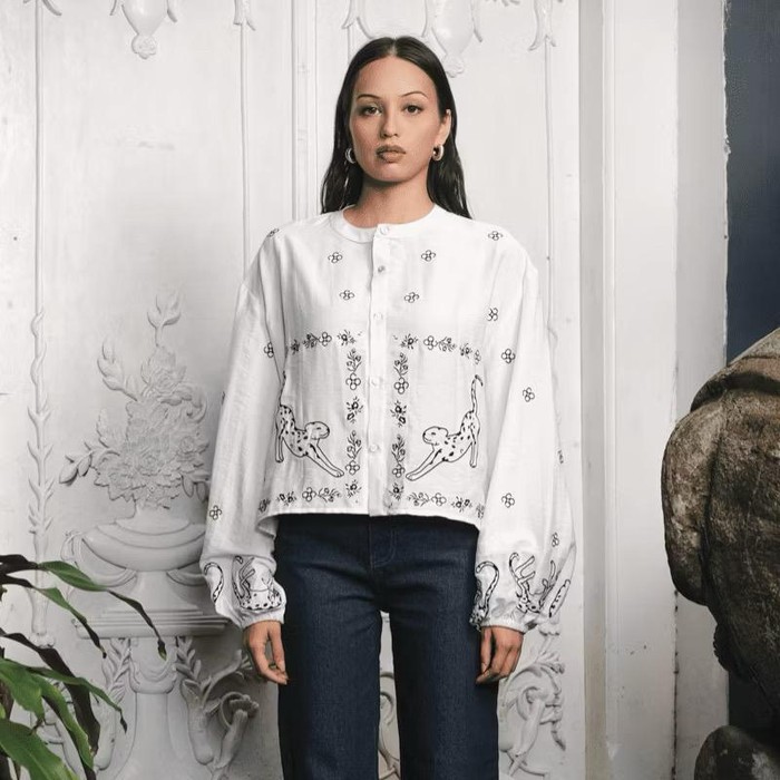 Matisse Gilly Bohemian Top Blouse dari brand Kyrra menghadirkan blouse berwarna putih dengan motif big cat serta elemen bunga yang ditampilkan dengan gaya line art minimalis.