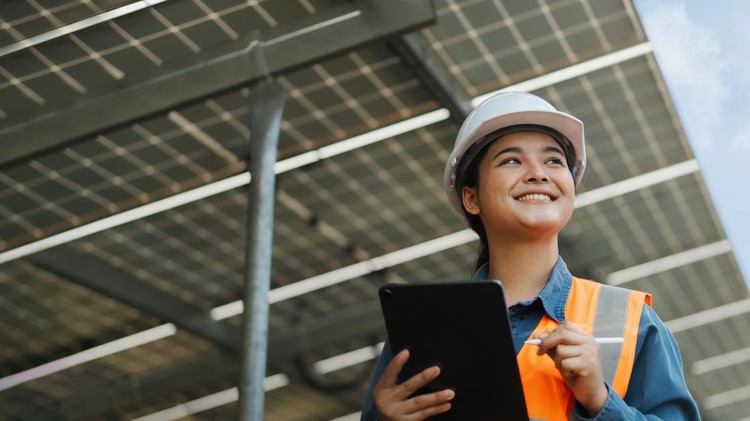 Female electrical engineer wearing hard hat using laptop checking solar panel farm equipment&period; Eco-friendly energy&period; Renewable clean energy technology concept&period;