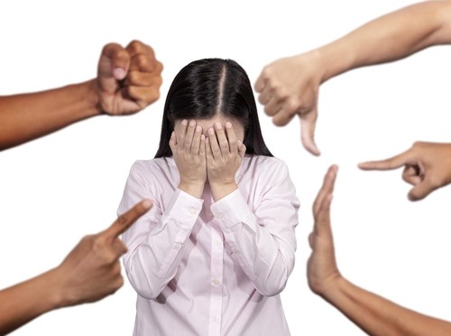 woman covered her face with regret for being bullying , sexism , racism and hate surrounded by hands mocking her, scoffing with offended at social of workplace