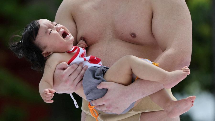 Pegulat sumo amatir menggendong bayi selama 'Nakizumo' alias kontes sumo bayi menangis di kuil Sensoji di Tokyo, Jepang, Sabtu (25/4/2026). (REUTERS/Issei Kato)