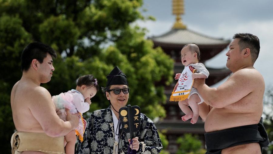 Pegulat sumo amatir menggendong bayi selama 'Nakizumo' alias kontes sumo bayi menangis di kuil Sensoji di Tokyo, Jepang, Sabtu (25/4/2026). (REUTERS/Issei Kato)