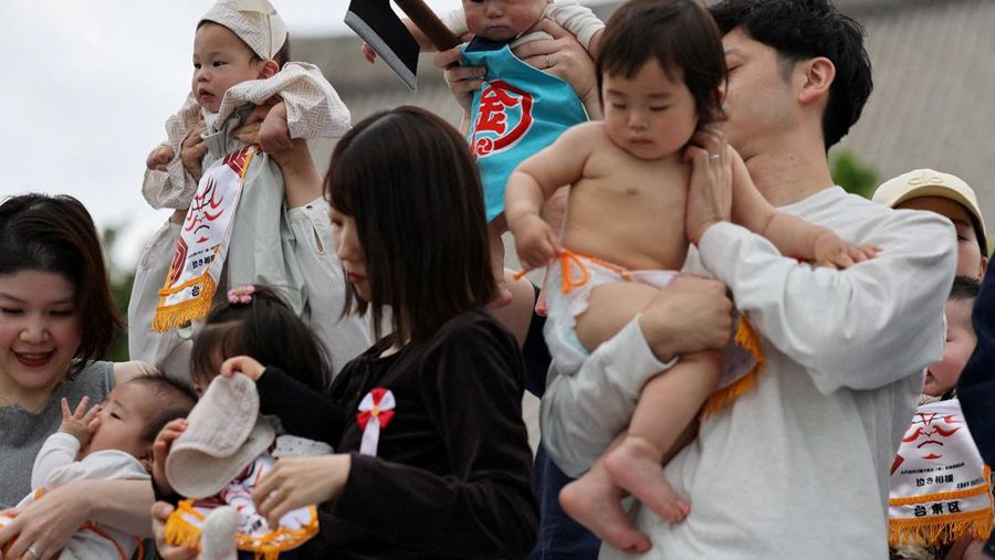 Pegulat sumo amatir menggendong bayi selama 'Nakizumo' alias kontes sumo bayi menangis di kuil Sensoji di Tokyo, Jepang, Sabtu (25/4/2026). (REUTERS/Issei Kato)