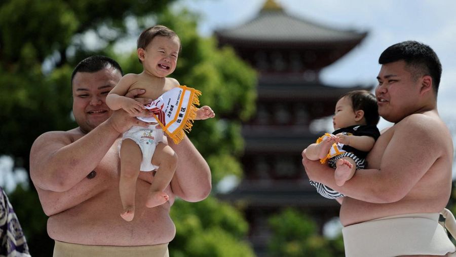 Pegulat sumo amatir menggendong bayi selama 'Nakizumo' alias kontes sumo bayi menangis di kuil Sensoji di Tokyo, Jepang, Sabtu (25/4/2026). (REUTERS/Issei Kato)