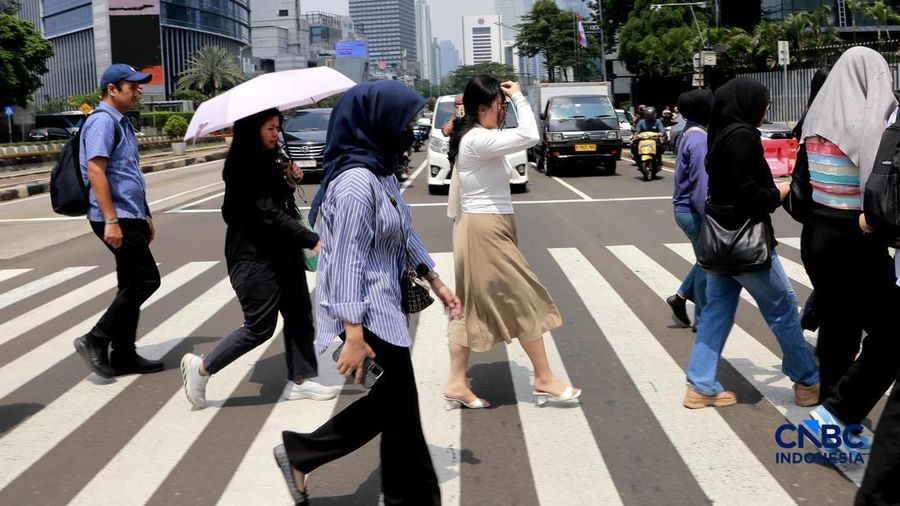 Warga melangkah dengan menutup kepala untuk berlindung dari terik mentari di Sudirman, Jakarta, Rabu (29/4/2026). (CNBC Indonesia/Muhammad Sabki)