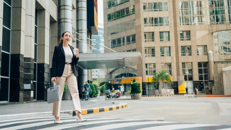 Young businesswoman walking across a pedestrian crossing in the financial district&comma; holding a takeaway coffee and a laptop bag&comma; going to work
