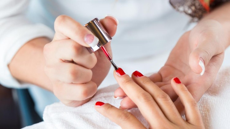Professional manicurist applying red nail polish to clients hands