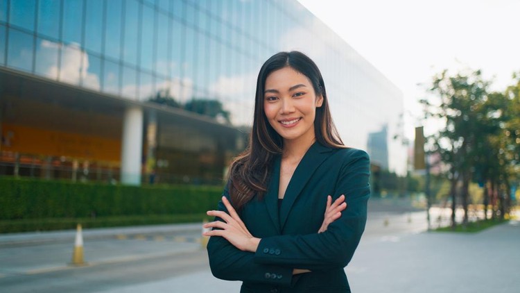 Portrait of happy beautiful young Asian businesswoman in business suit looking at camera and smiling&comma; Confident executive director standing and posing with arms crossed&comma; Professional female manager working at modern office building&comma; Business people at work