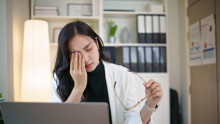 Tired office worker overwhelmed by tasks&comma; taking a break while holding eyeglasses and rubbing her face&period;