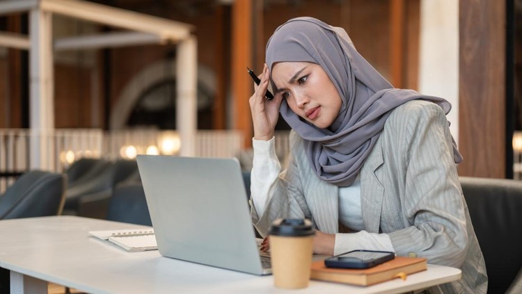 Troubled asian muslim woman student holding head looking at laptop sitting with book at cafe table&period; Everyday life&comma; Modern tech&comma; Chilling Outdoors&period;