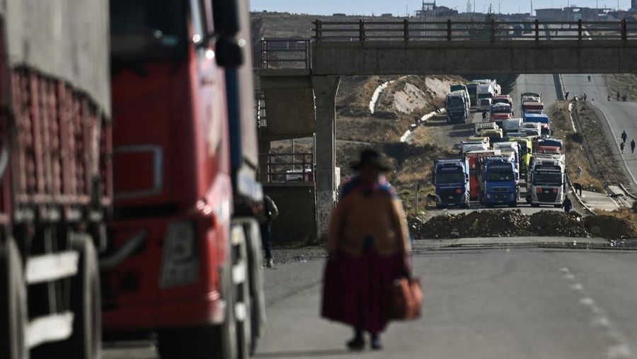 Seorang wanita melangkah di antara truk-truk nan terhenti selama berhari-hari lantaran para pengunjuk rasa memblokir jalan raya utama, menuntut pengunduran diri Presiden Rodrigo Paz di tengah krisis ekonomi dan bahan bakar nan sedang berlangsung, di Apacheta, Bolivia, 13 Mei 2026.