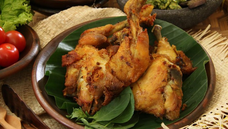 Ayam Penyet Sambal Hijau&comma; a popular main dish in Surabaya&comma; East Java&period; Marinated chicken pieces lightly smashed then deep fried&semi; served with green chili paste&comma; fried marinated tofu and tempeh&comma; and fresh vegetables&period; The chicken&comma; tofu&comma; tempeh&comma; and vegetables are served on traditional earthenware crockery while the green chili paste is served on a stoneware mortar&period; This is a close-up view of the fried chicken&period;