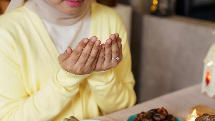 Muslim woman in hijab making dua before breaking fast during Ramadan&period; Spiritual moment before iftar meal at home with traditional food on the table&comma; representing Islamic culture&comma; faith&comma; gratitude&comma; and family dining during the holy month&period;
