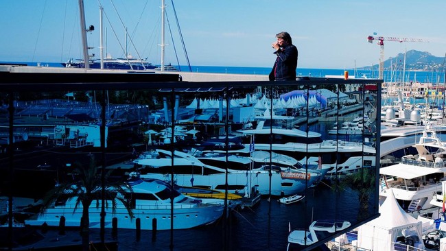 A person drinks coffee on a terrace overlooking the port and yachts during the 79th Cannes Film Festival in Cannes, France, May 18, 2026. REUTERS/Manon Cruz