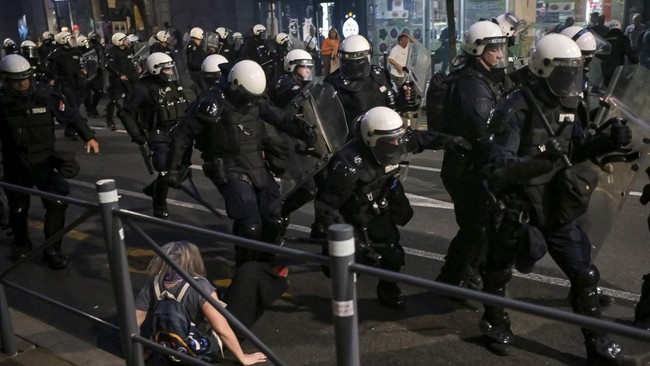 A police officer kicks a protestor on the ground as they clash with riot police outside Serbia's parliament building during clashes that erupt at the end of an anti-government protest decrying corruption and calling for early elections following the